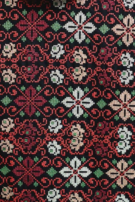 Close-up of colorful Palestinian Tatreez floral embroidery in red, white, and green on black fabric, showcasing intricate design