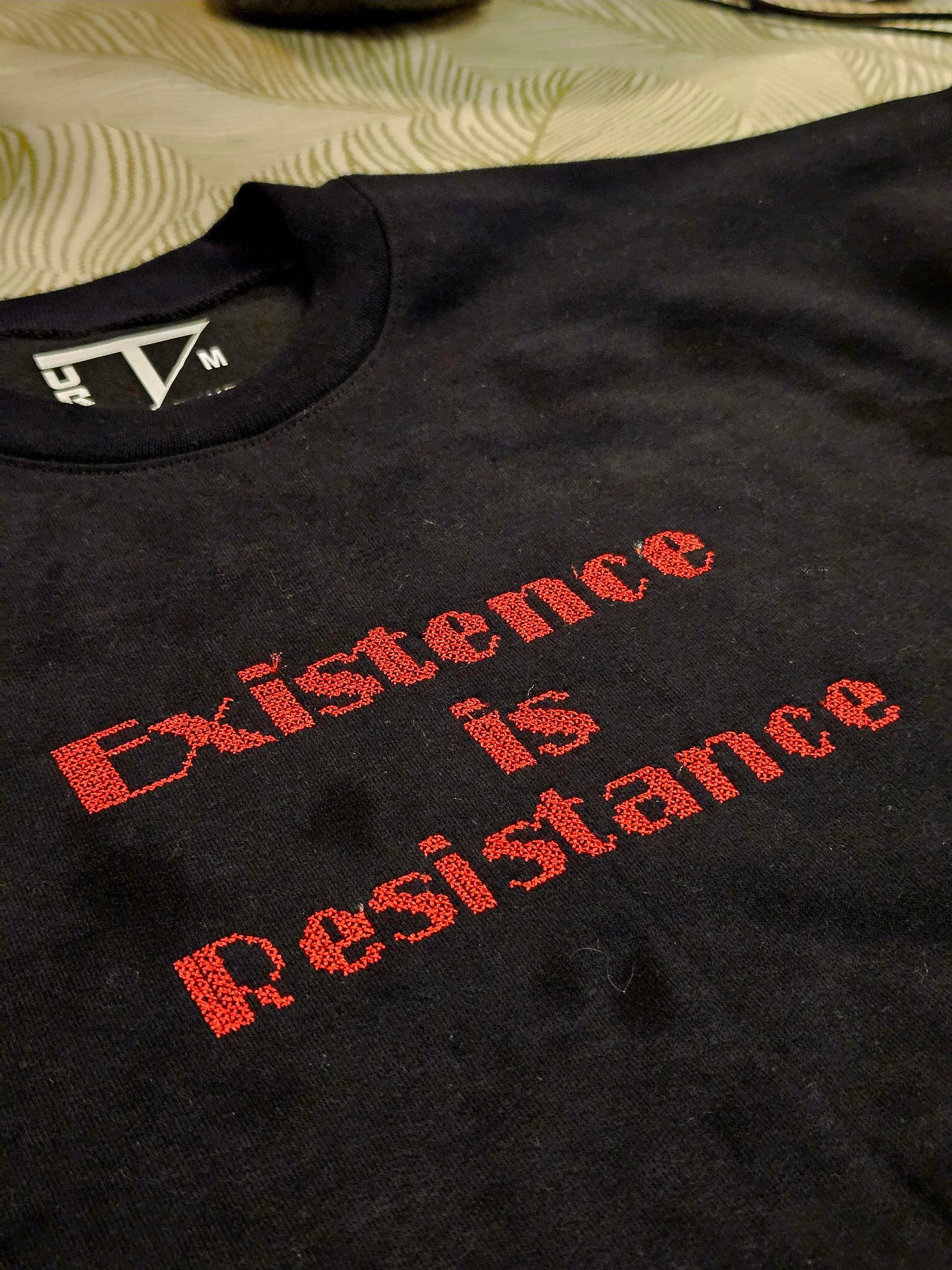 Close-up of Palestinian tatreez cross-stitch embroidery with the phrase Existence is Resistance on a black sweatshirt.
