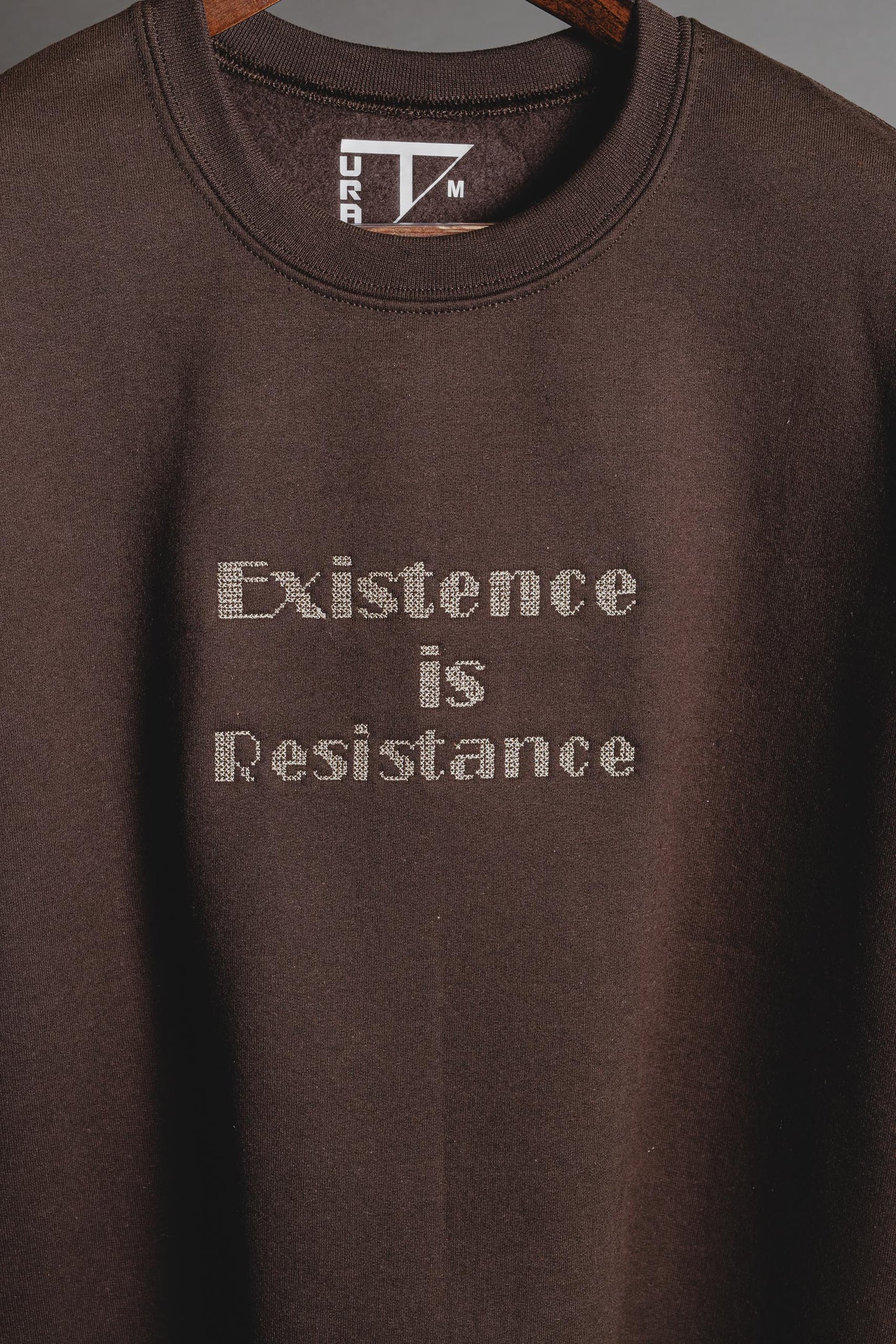 Close-up of Palestinian tatreez cross-stitch embroidery with the phrase Existence is Resistance on a black sweatshirt.