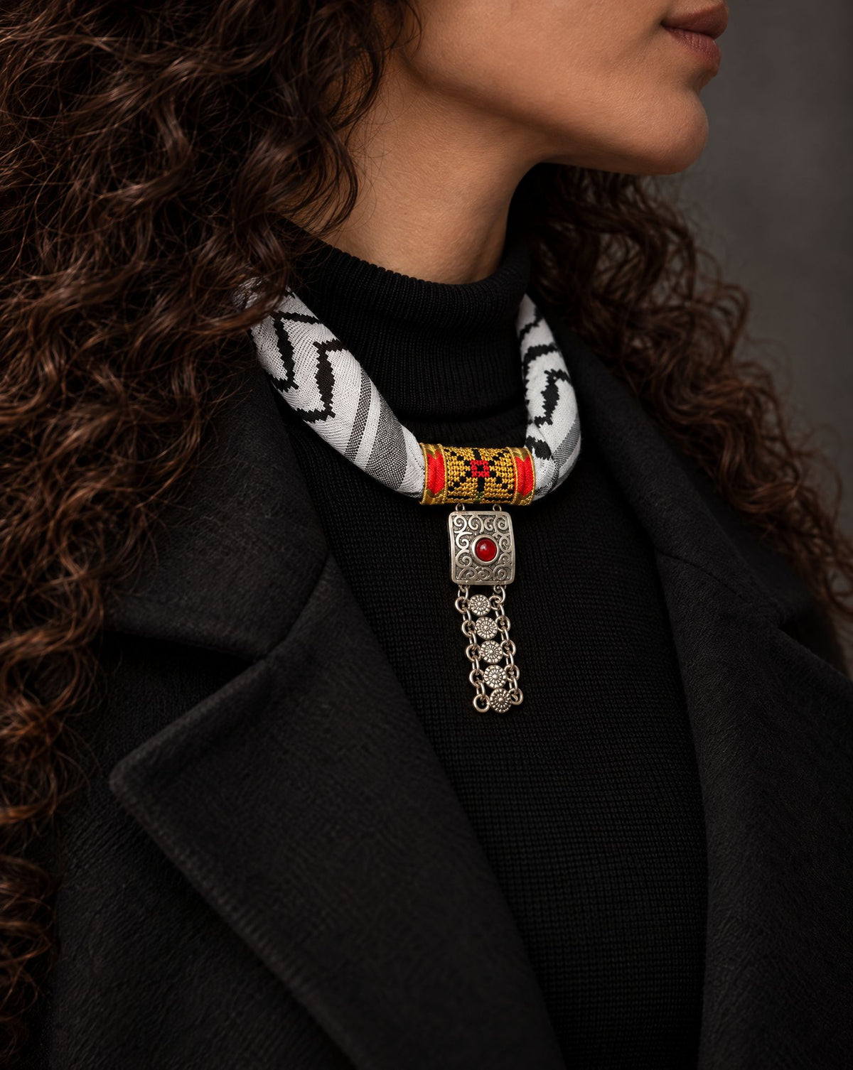 Woman wearing a Palestinian keffiyeh scarf necklace with gold tatreez band and square silver-tone pendant with red stone