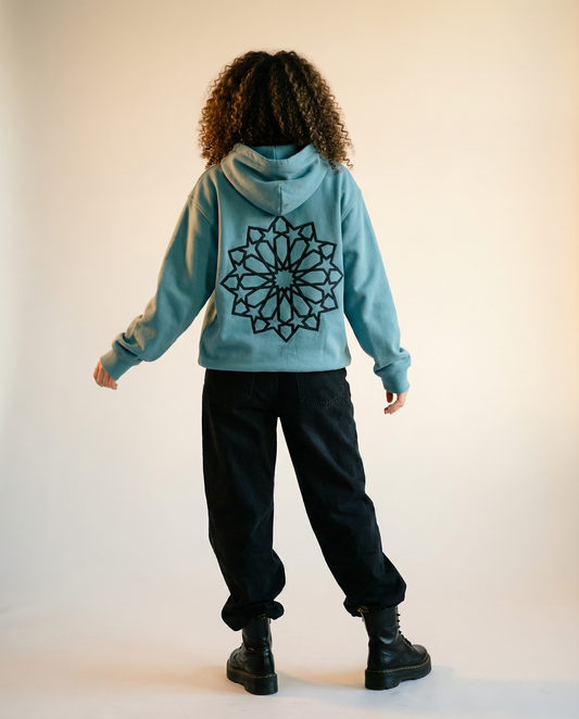 Back view of a model wearing the green Al-Aqsa Window Hoodie with black denim pants