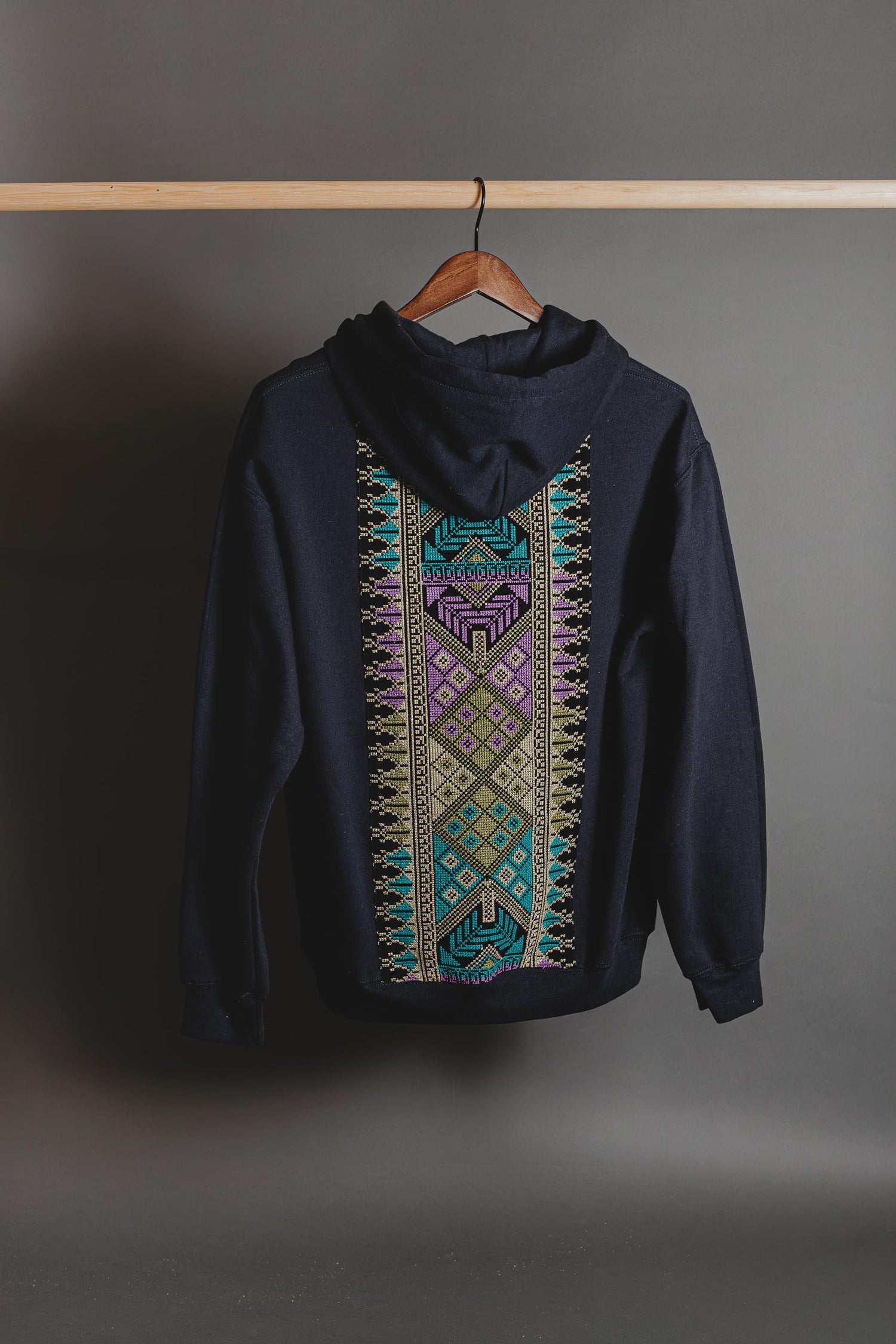Black hoodie with colorful geometric pattern on a hanger against a gray background