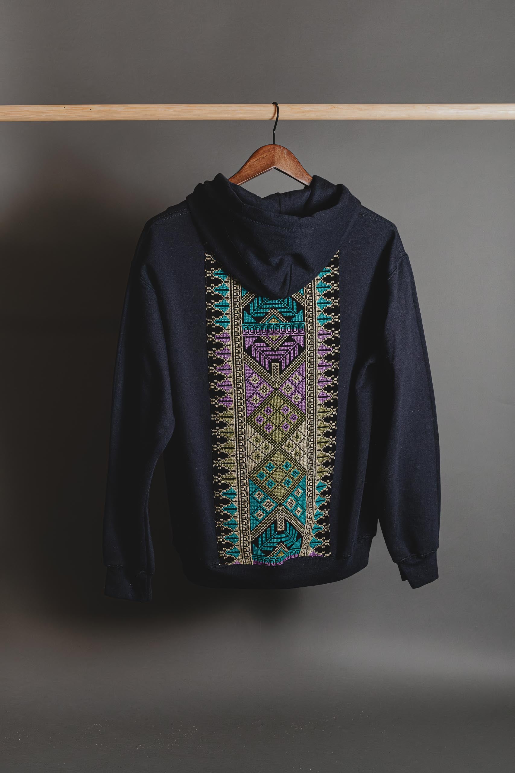 Black hoodie with colorful geometric pattern on a hanger against a gray background