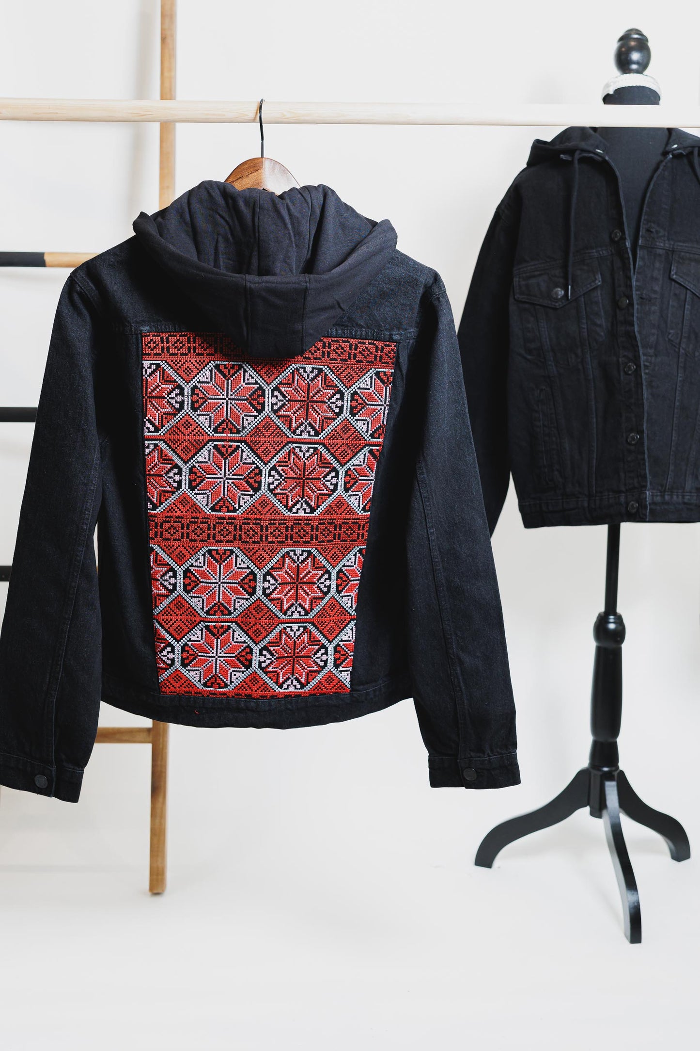 Black denim hooded jacket with vibrant Palestinian Tatreez embroidery on the back, showcasing traditional craftsmanship and cultural heritage