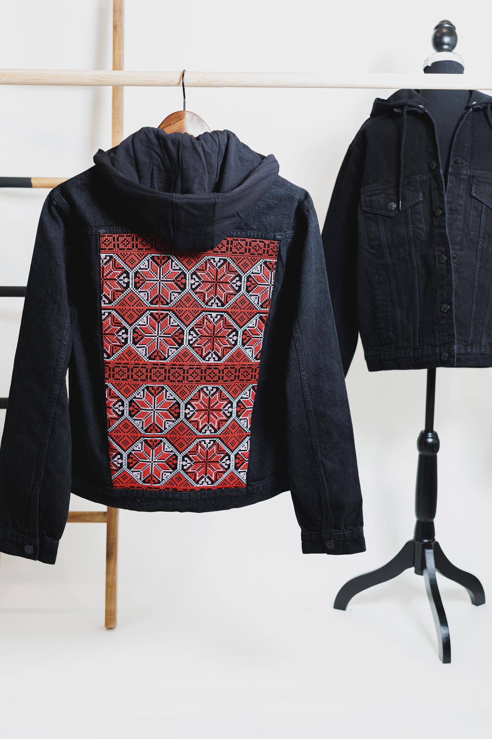 Black denim hooded jacket with vibrant Palestinian Tatreez embroidery on the back, showcasing traditional craftsmanship and cultural heritage