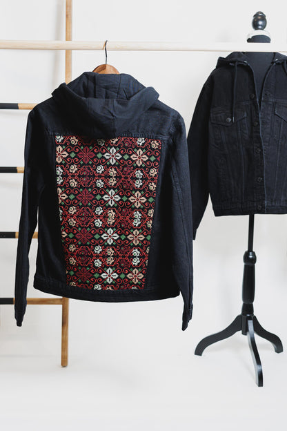 Black unisex denim jacket with hood and floral Tatreez embroidery on the back, showcasing Palestinian culture.