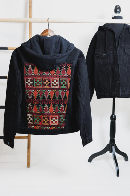 A black unisex denim jacket with a hood, featuring geometric Tatreez embroidery on the back. showcasing Palestinian heritage and modern style