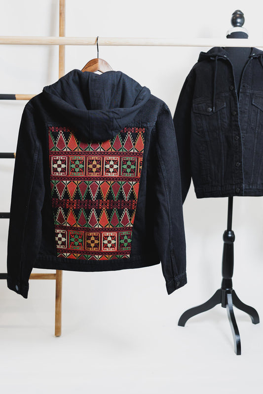 A black unisex denim jacket with a hood, featuring geometric Tatreez embroidery on the back. showcasing Palestinian heritage and modern style