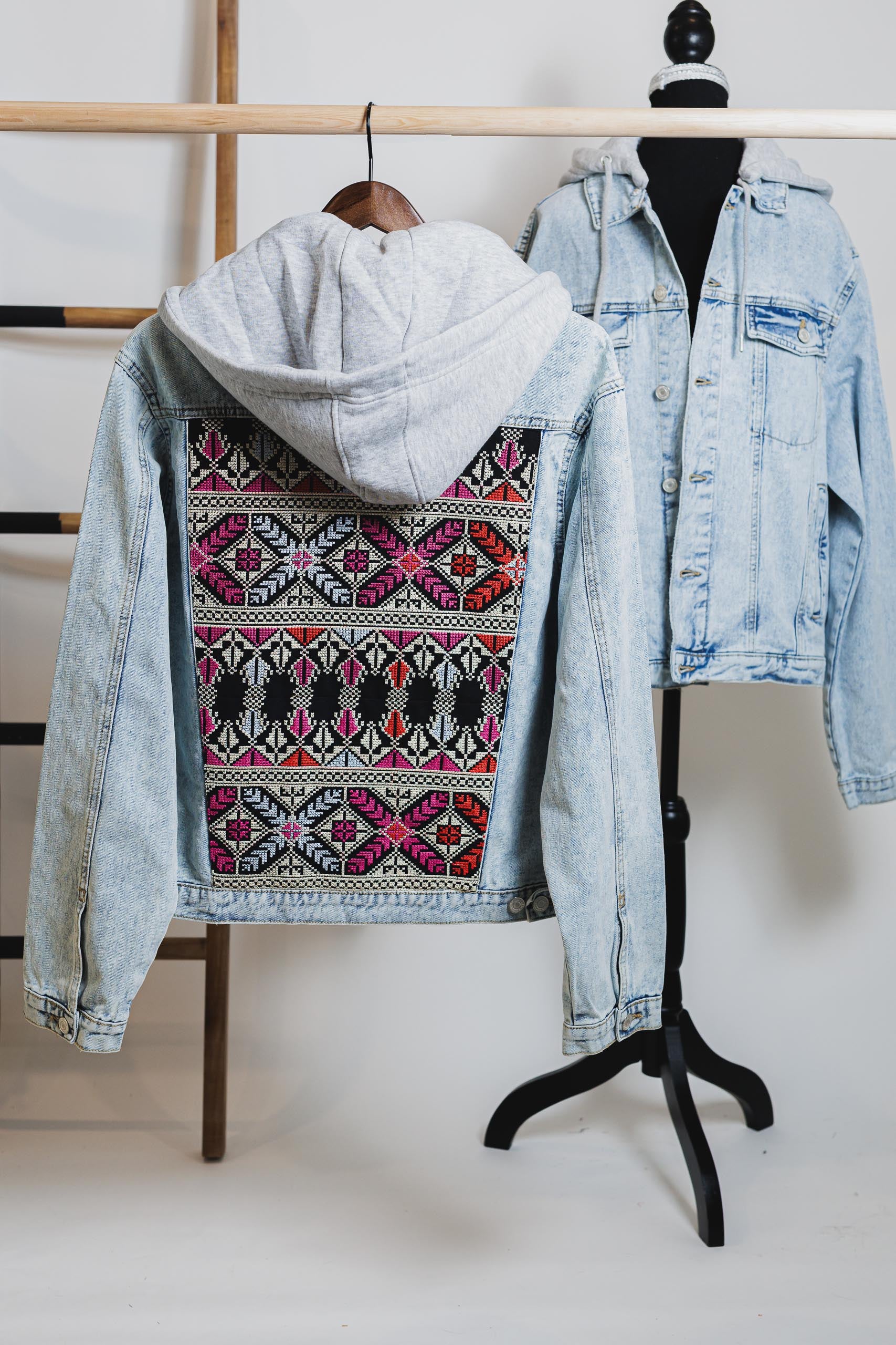 Unisex light blue denim jacket with gray hood, featuring bold embroidered Palestinian Tatreez design on back