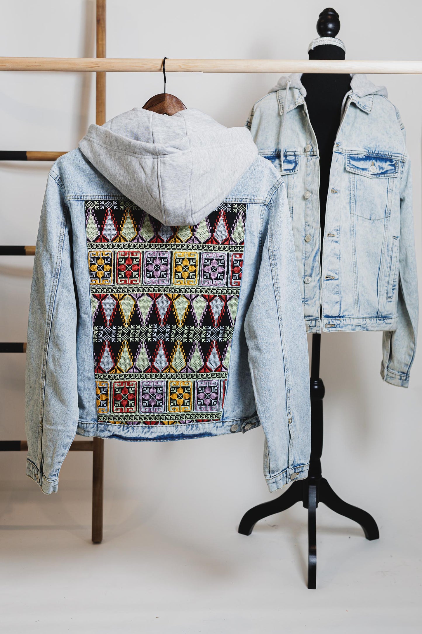 Unisex light blue denim jacket with gray hood and vibrant embroidered Palestinian Tatreez design on back