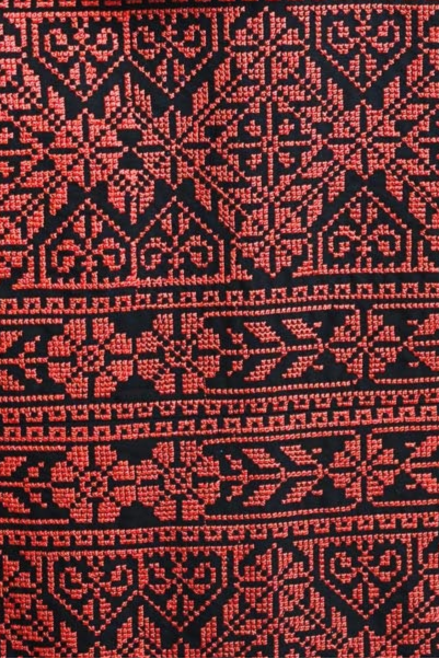 Close-up of vibrant red Palestinian Tatreez embroidery design on black fabric, showcasing traditional motifs